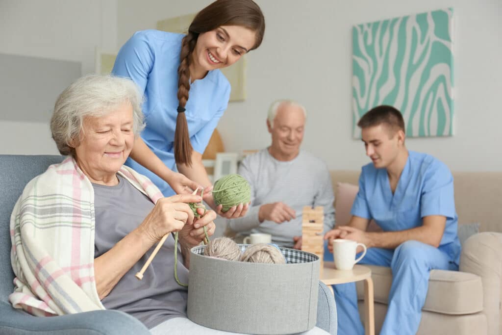 Senior woman knitting with assistance of her caregiver